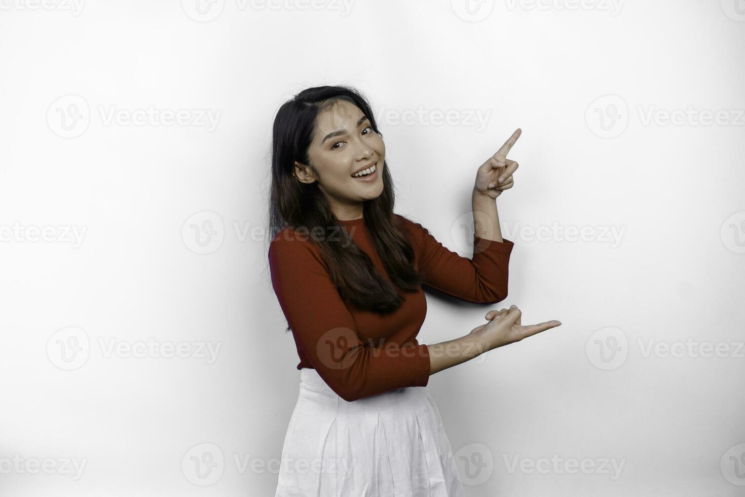 opgewonden Aziatisch vrouw vervelend rood t-shirt, richten Bij de kopiëren ruimte naast haar, geïsoleerd door wit achtergrond foto