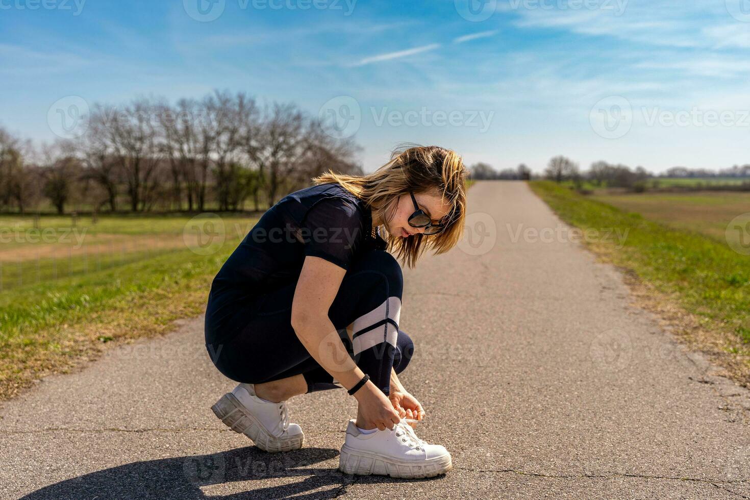 schattig atleet vrouw koppelverkoop haar schoenen gedurende een training Aan een land weg foto