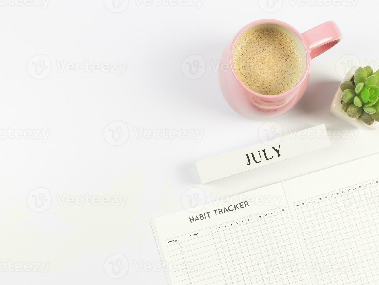 vlak leggen van gewoonte tracker boek, houten kalender juli, roze kop van zwart koffie en sappig fabriek pot Aan wit achtergrond met kopiëren ruimte. foto