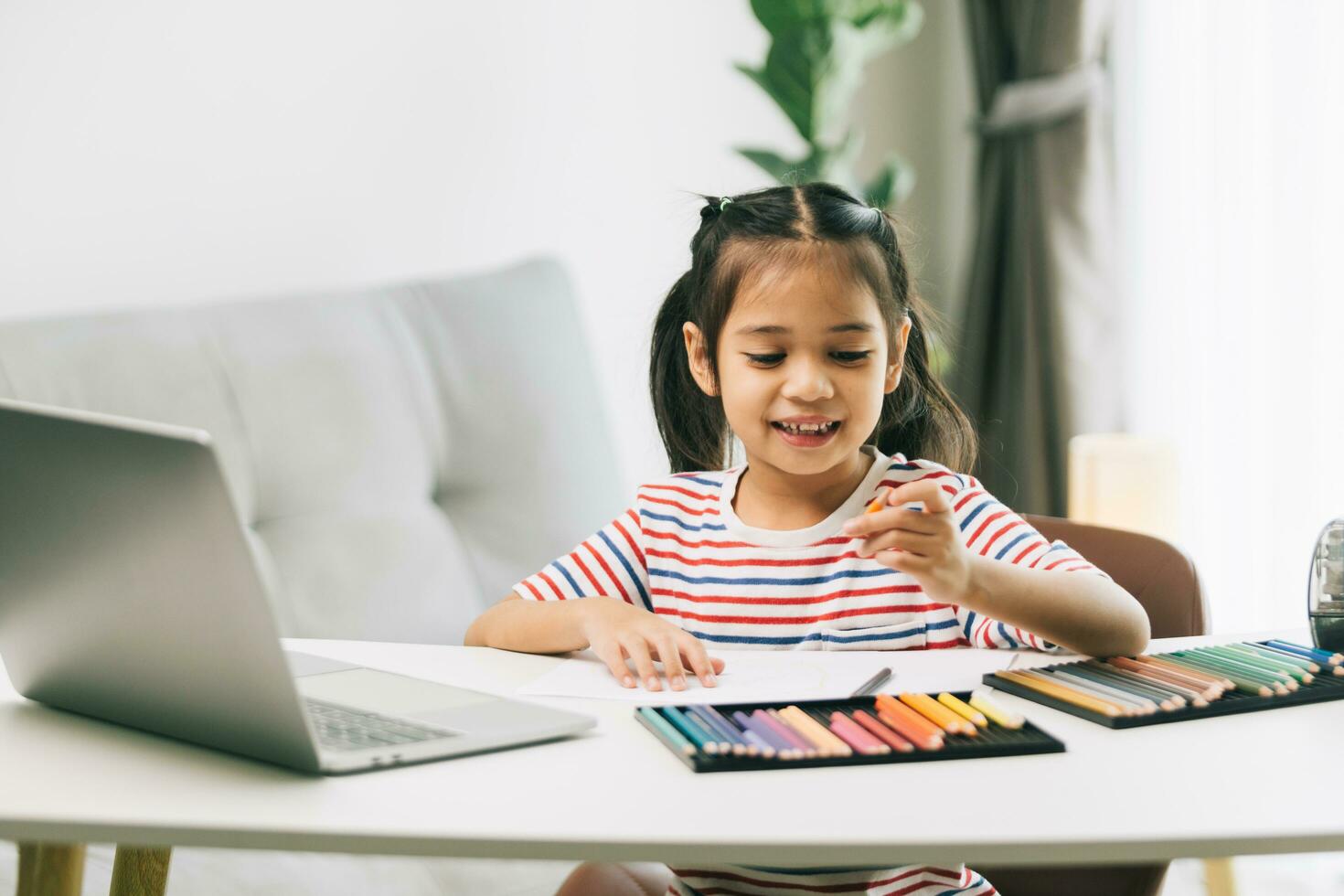 schattig Aziatisch kind meisje gebruik makend van laptop en kleur potloden Bij huis foto