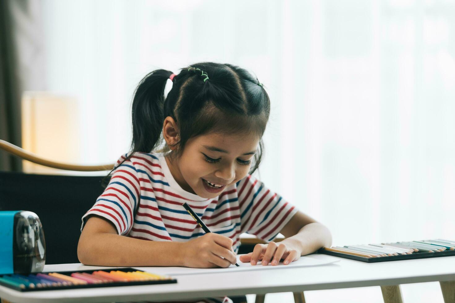 schattig Aziatisch kind meisje tekening met potloden Bij huis. foto