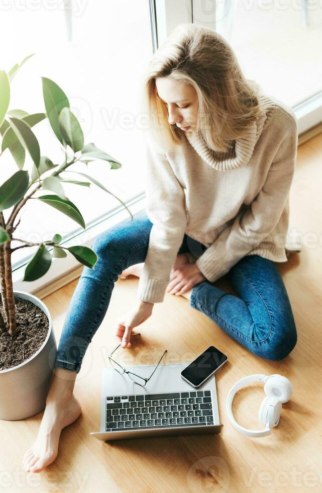 jong vrouw gebruik makend van haar laptop terwijl zittend Aan de verdieping Bij huis. foto