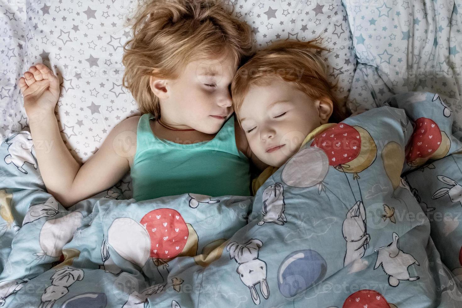 twee kleine zusjes en zusjes die in een omhelzing in bed slapen onder één deken foto