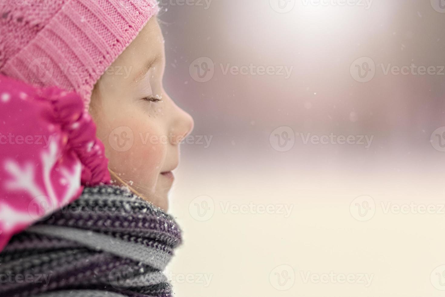 portret van een klein meisje in roze close-up. een kind geniet van de sneeuwval. Kerstvakantie foto