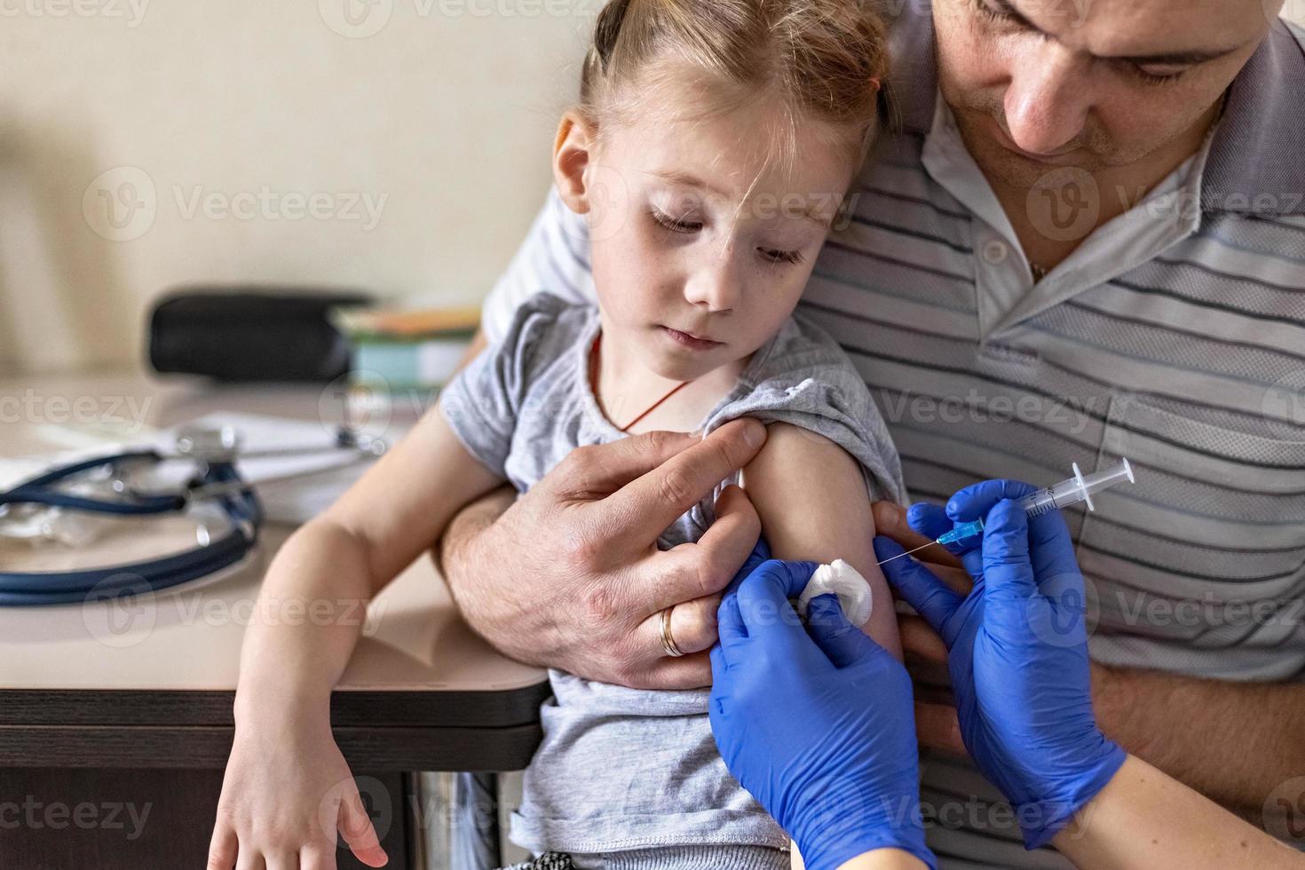 een klein meisje met haar vader in de spreekkamer van de kliniek wordt ingeënt tegen het coronavirus. het concept van vaccinatie, immunisatie, preventie tegen covid-19. foto