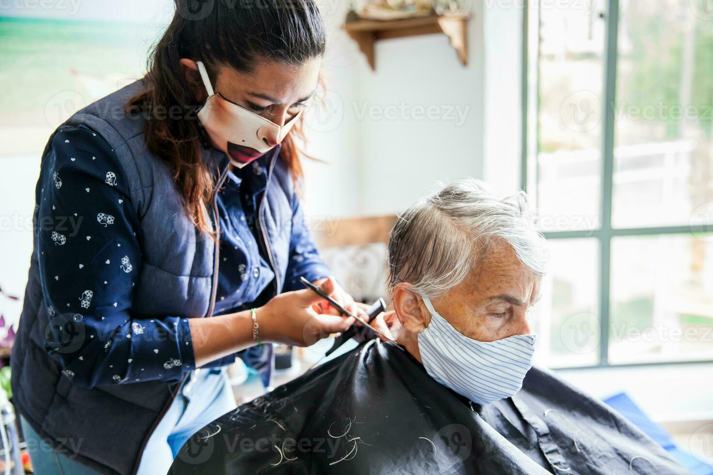 senior vrouw krijgen een kapsel Bij huis gedurende covid19 pandemisch vervelend gezicht masker foto