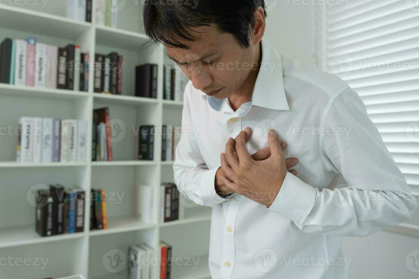 hand- houden borst met hart aanval symptomen, Aziatisch Mens werken moeilijk hebben borst pijn veroorzaakt door hart ziekte, lek, dilatatie, vergroot coronaire hart, druk op Aan de borst met een pijnlijk uitdrukking foto
