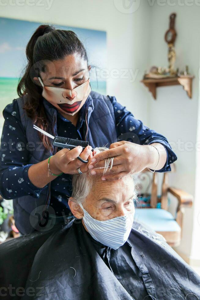 senior vrouw krijgen een kapsel Bij huis gedurende covid19 pandemisch vervelend gezicht masker foto