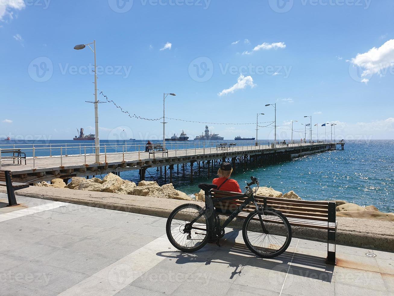 een man zit op een bankje achter een fiets kijkt naar de zee op de Molos-promenade in limassol, cyprus foto