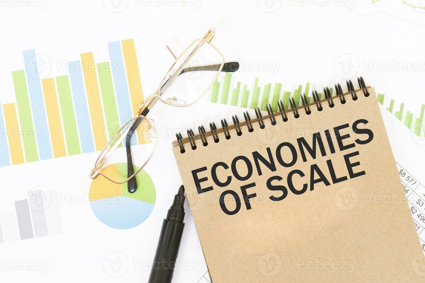 in een ambacht kleur notitieboekje is een economieën van schaal inscriptie, De volgende naar potloden, bril, grafieken en diagrammen. foto