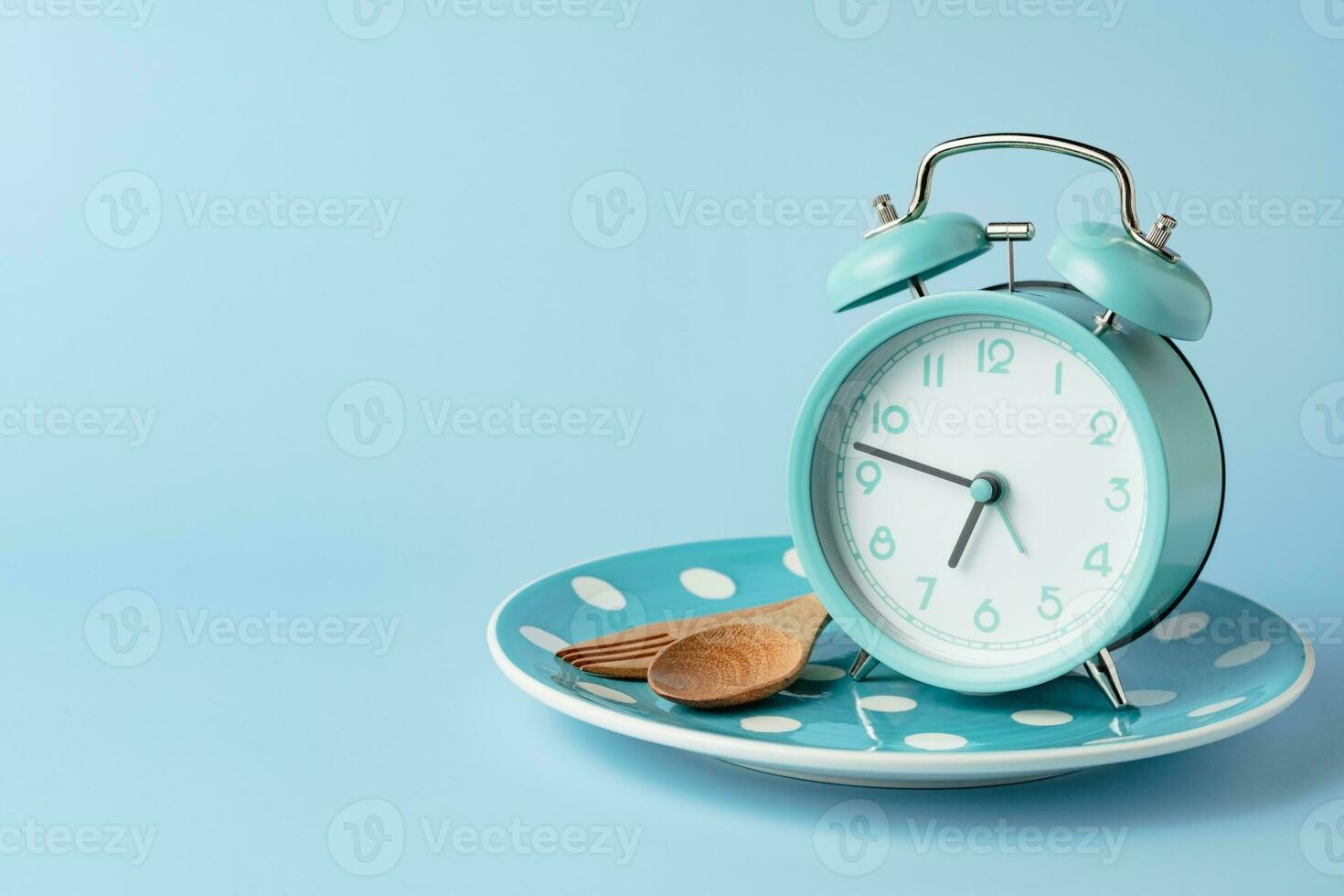een alarm klok Aan een leeg bord en bestek reeks tegen blauw achtergrond foto