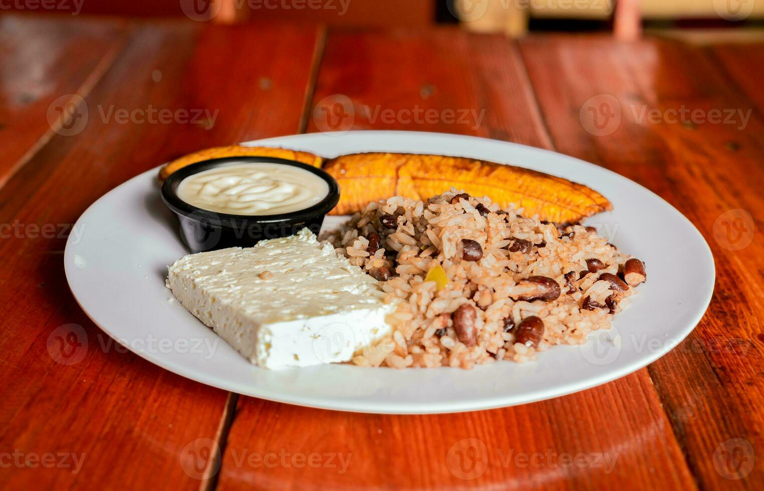 traditioneel gallo pinto maaltijd met maduro en kaas geserveerd. galopperen bord met kaas en maduro Aan houten tafel. Nicaraguaanse voedsel concept foto