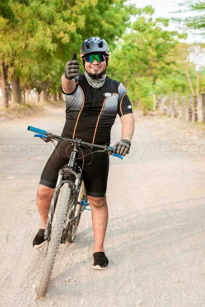 fietser geven duimen omhoog Aan een weg. professioneel fietser aan het doen OK gebaar Aan zijn fiets foto