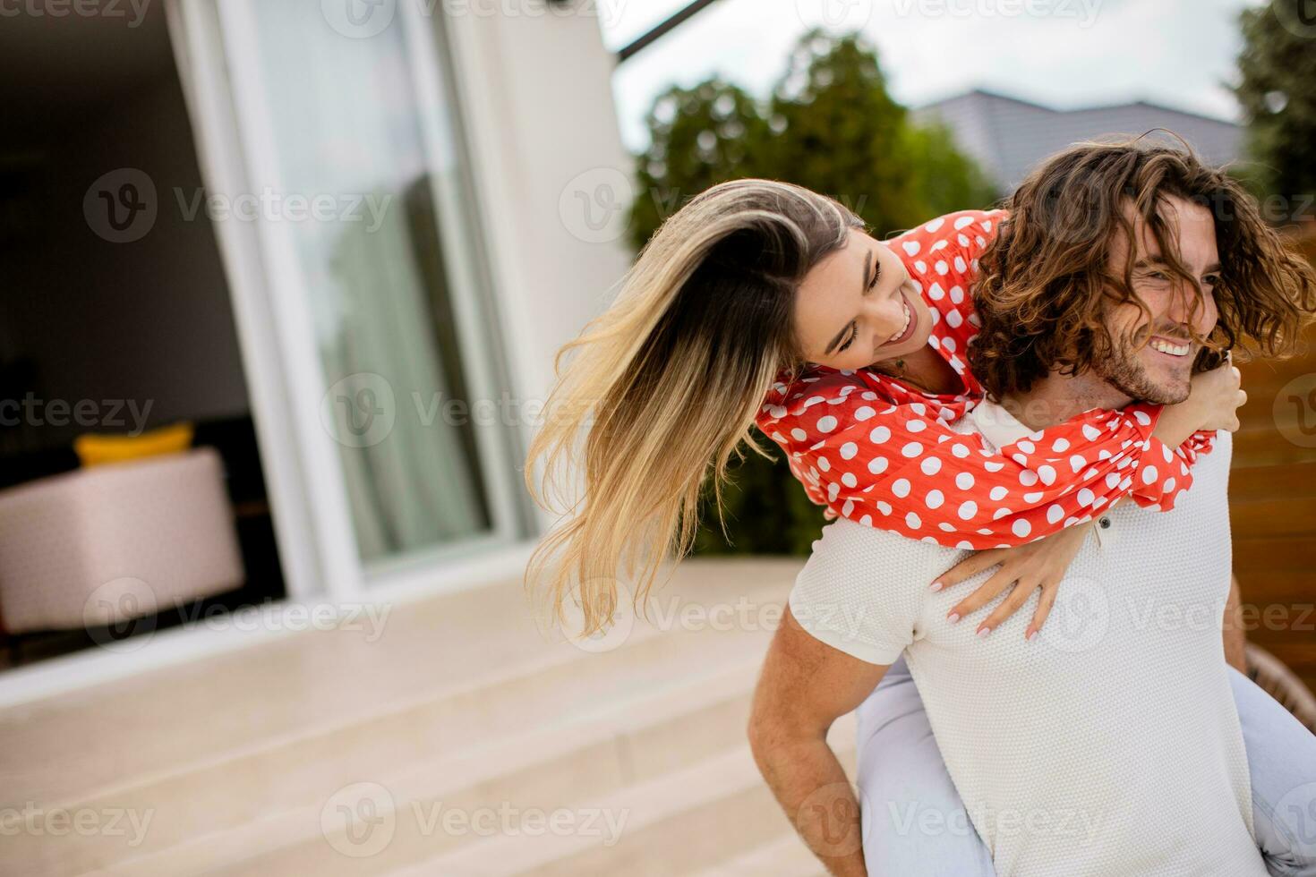 knap lang haar- Mens draag- de jong vrouw Aan zijn terug in voorkant van steen huis foto