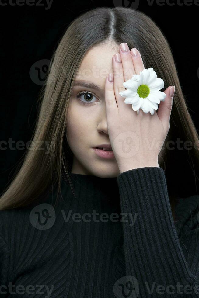 een mooi meisje met natuurlijk schoonheid houdt een wit bloem in de buurt haar oog. jong meisje met een wit chrysant. foto