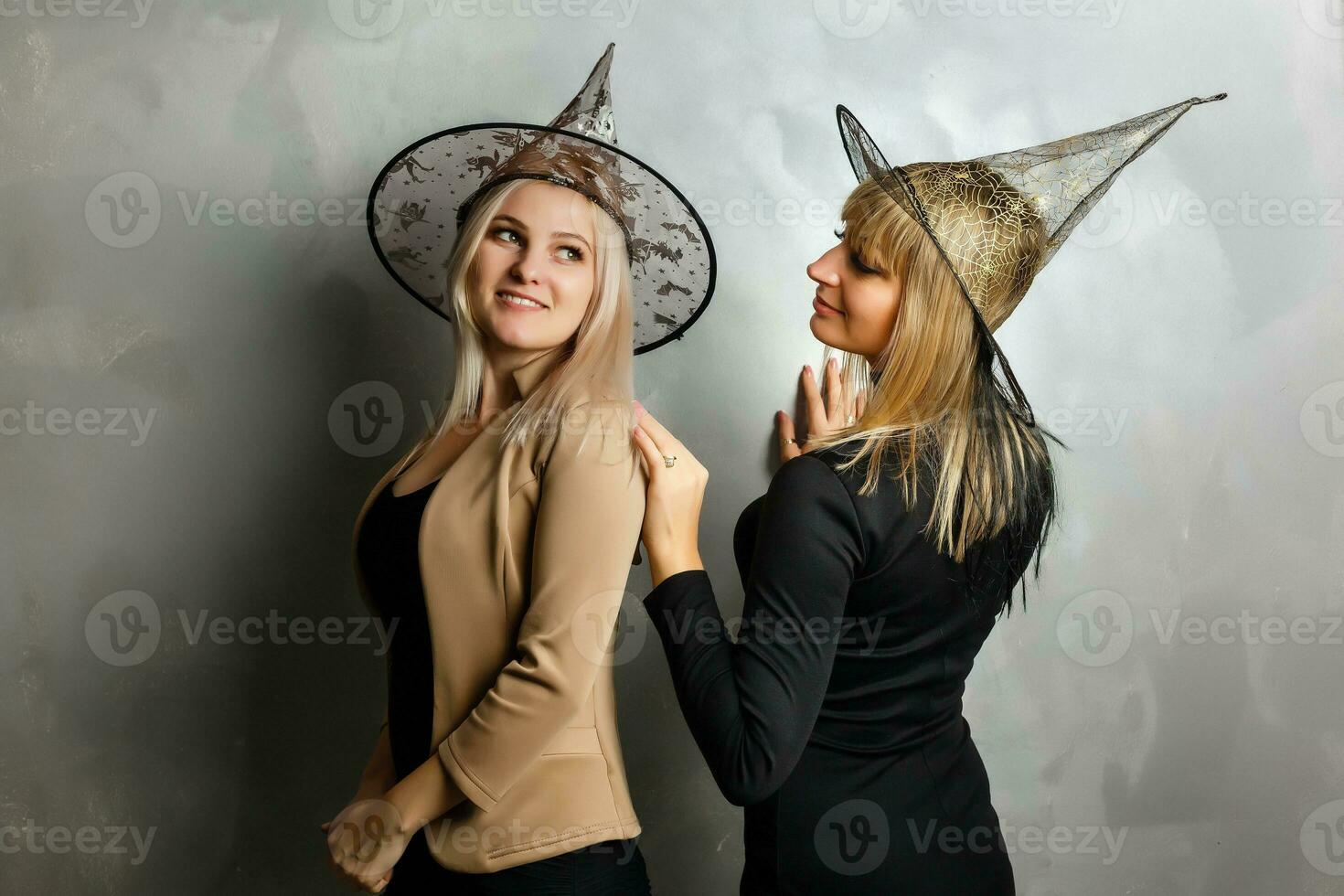 portret van twee gelukkig jong Dames in zwart heks halloween kostuums Aan partij over- grijs achtergrond. foto
