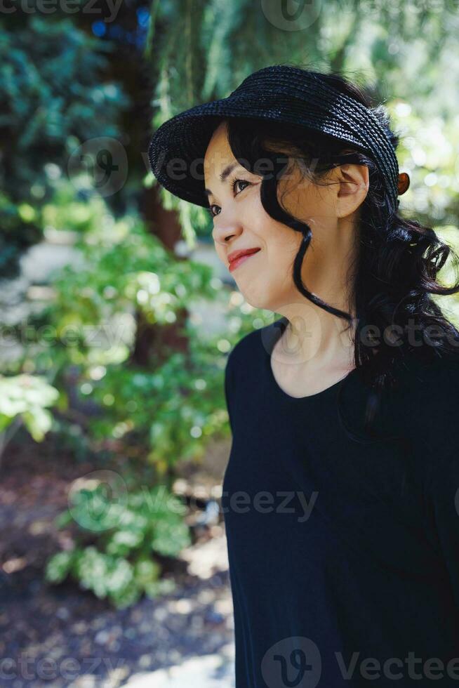 middelbare leeftijd Japans vrouw in zwart rietje zon rand hoed, zomer park foto