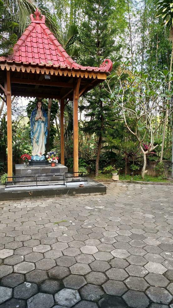 standbeeld van de maagd Maria onder een luifel met bomen in de achtergrond, in de jatiningsih Maria grot, jogjakarta, waar katholieken bidden, geven bedankt en verzenden verzoeken naar god foto