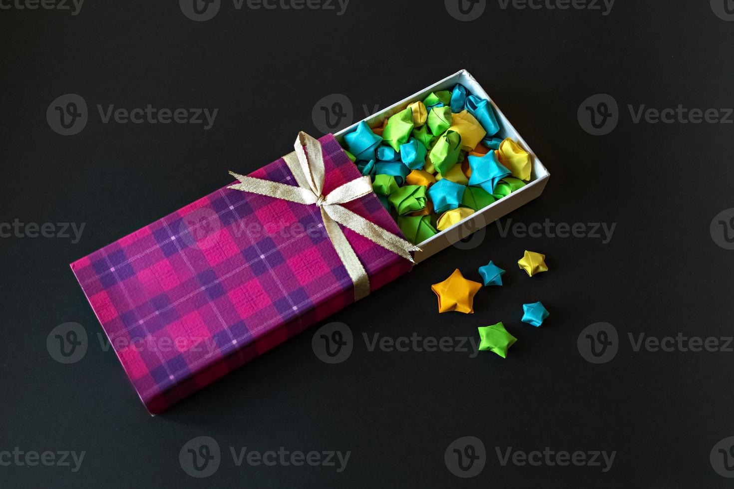 gekleurde geschenkdoos met satijnen strik met origami papieren sterren op zwarte achtergrond. cadeaus voor de feestdagen. foto