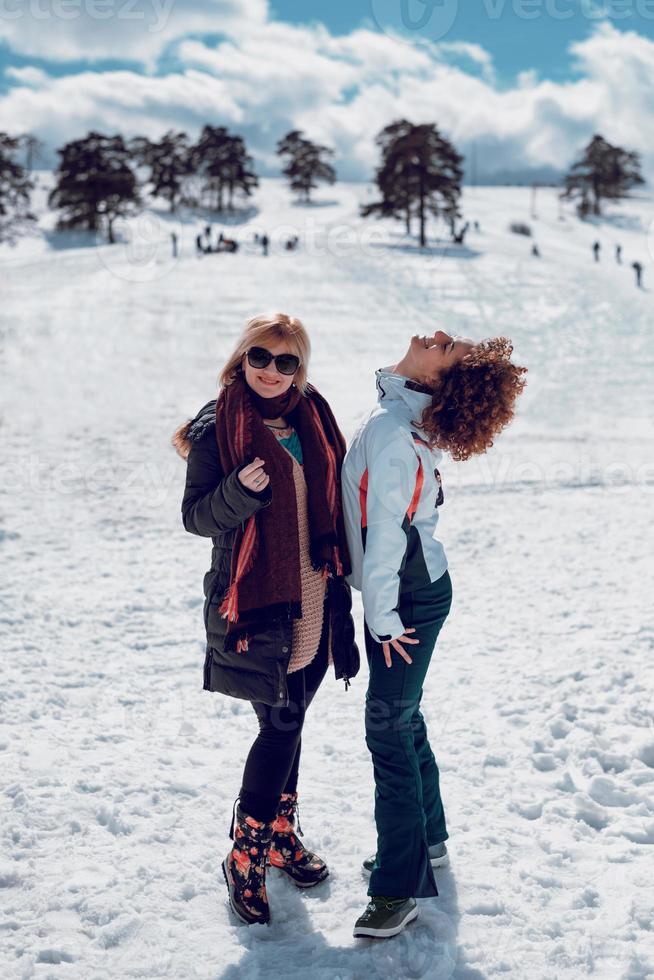 twee gelukkige vrouwen staan en hebben plezier in sneeuw op de zonnige winterdag. foto