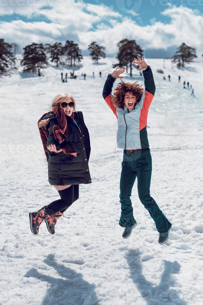 twee gelukkige vrouwen springen in de lucht en hebben plezier in sneeuw op de zonnige winterdag. foto