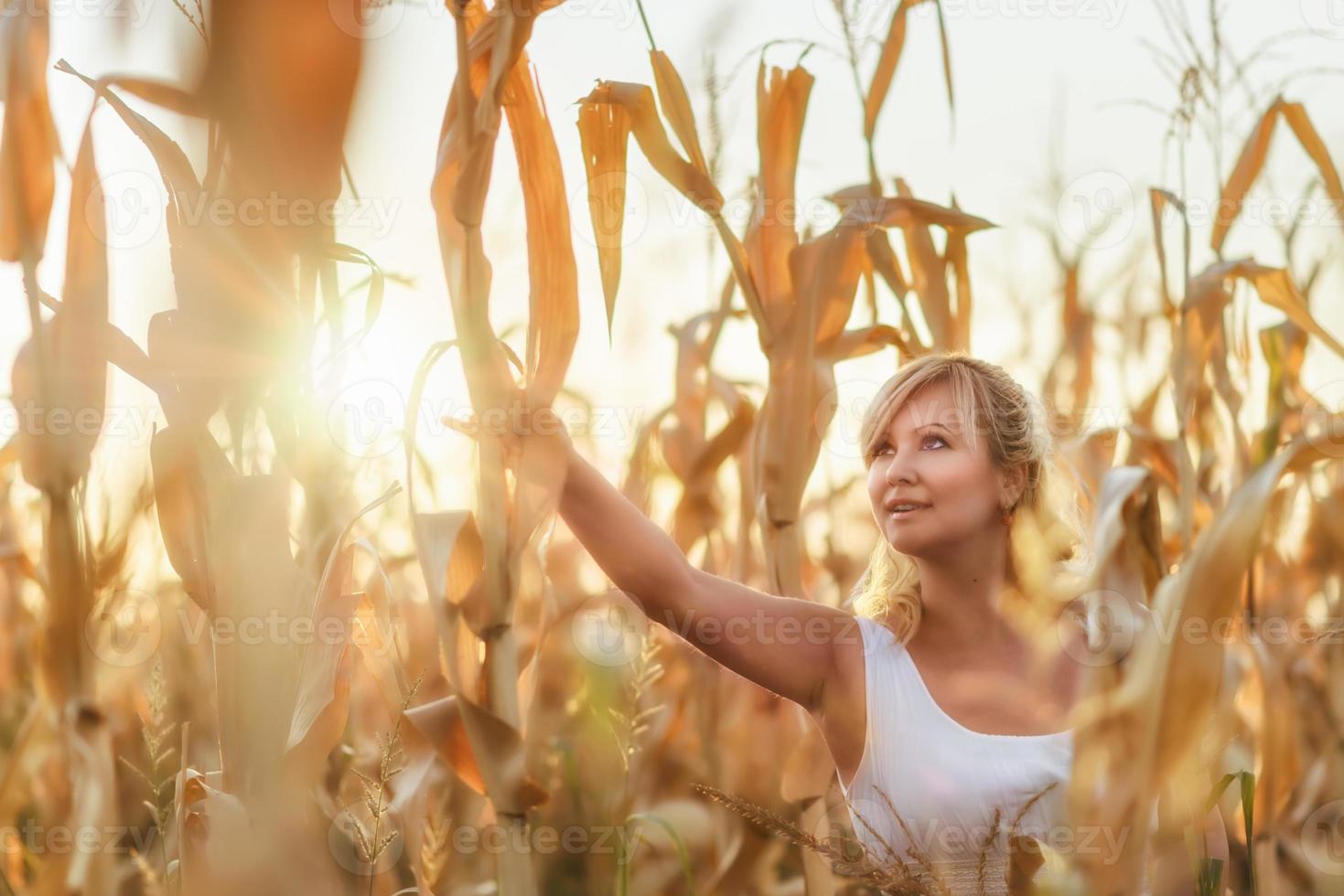 vrouw in een witte lange zomerjurk loopt op een korenveld en poseert in zonsondergangtijd. foto