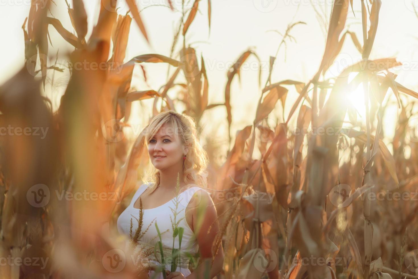 vrouw in een witte lange zomerjurk loopt op een korenveld en poseert in zonsondergangtijd. foto