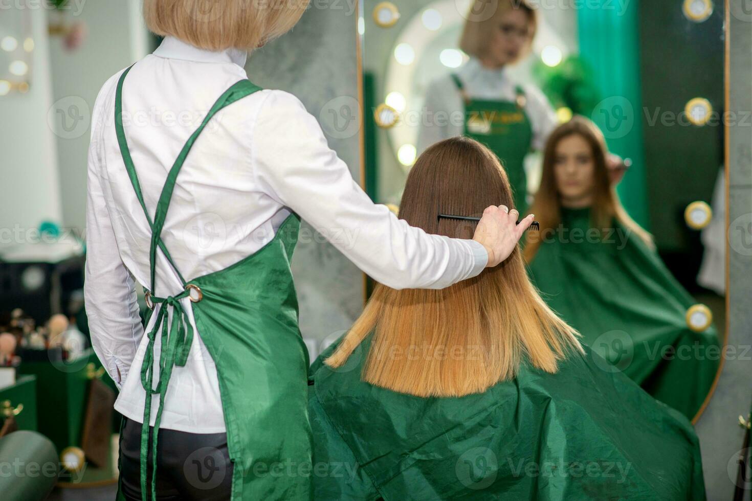 een vrouw kapper is kammen de lang bruin haar- van een jong vrouw Bij een salon. foto