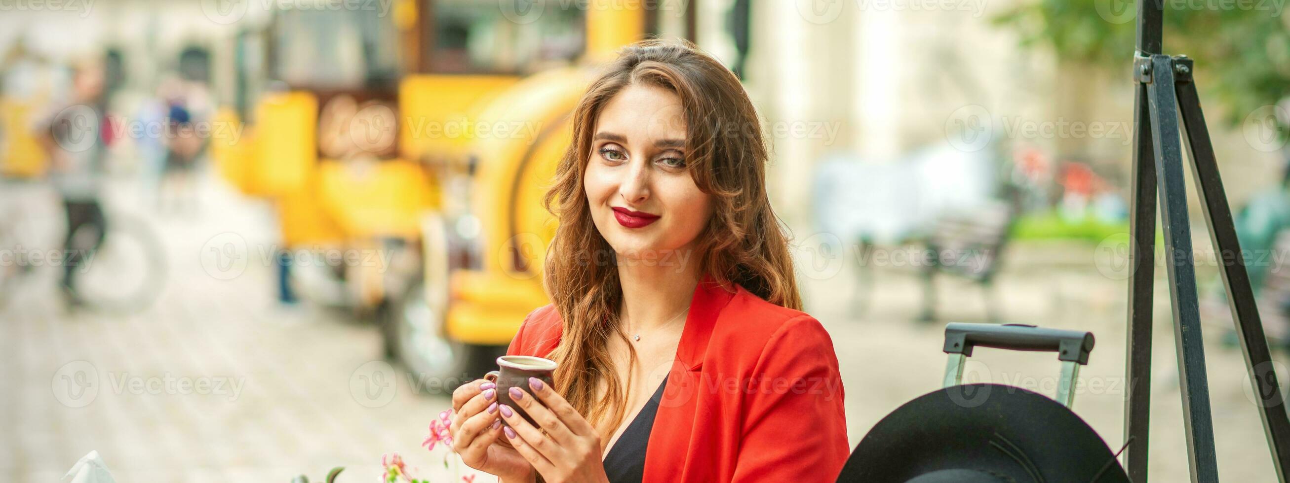 toerist jong Kaukasisch vrouw in rood jasje met koffie kop Bij de tafel in cafe buitenshuis. foto