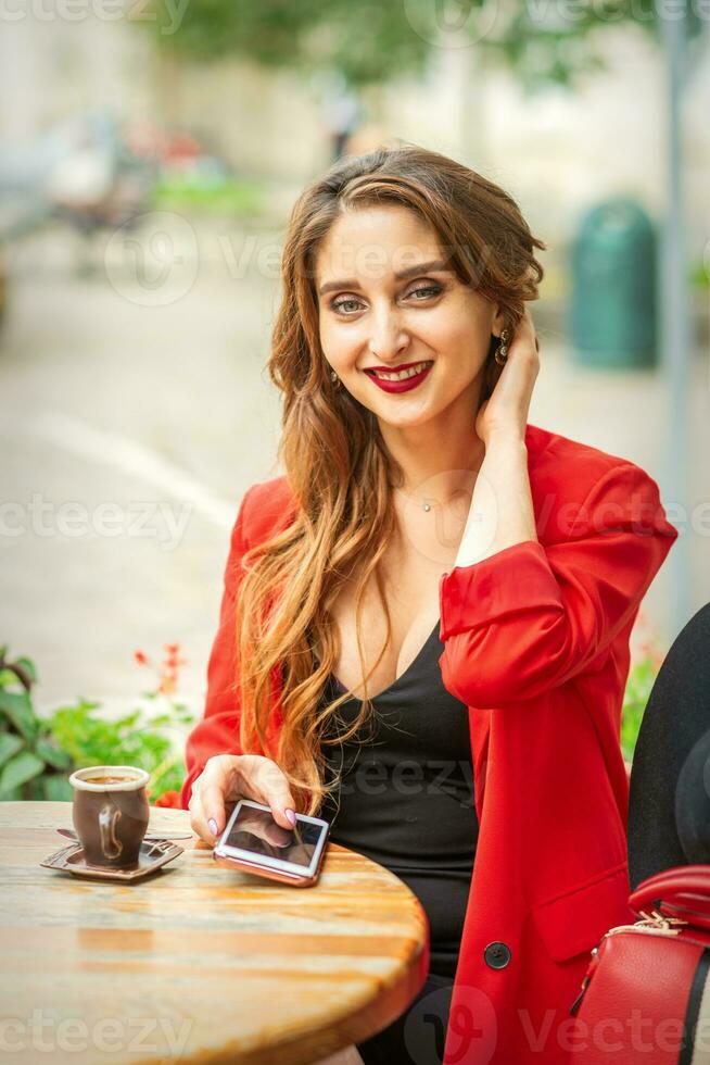 portret van een jong wit vrouw zittend Bij de tafel met een smartphone en op zoek Bij camera buitenshuis. foto