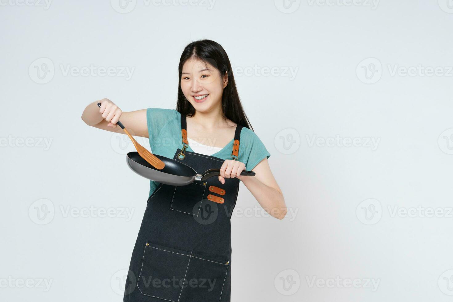 jong vrouw vervelend keuken schort Koken en Holding pan en spatel geïsoleerd Aan wit achtergrond. foto