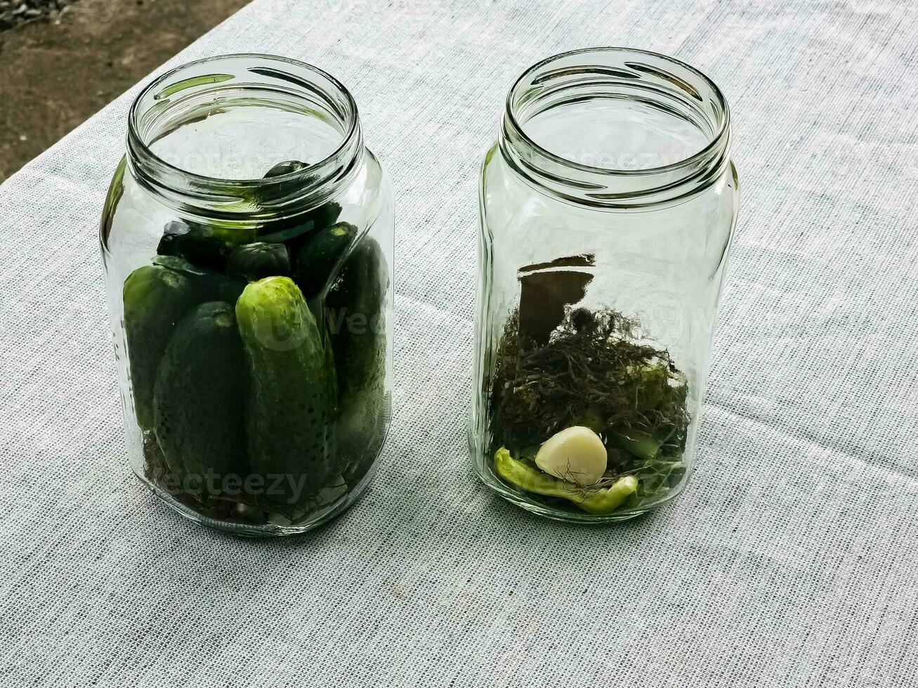 de werkwijze van beitsen komkommers voor de winter in glas potten. specerijen voor zouten zijn gelegd uit in potten. foto