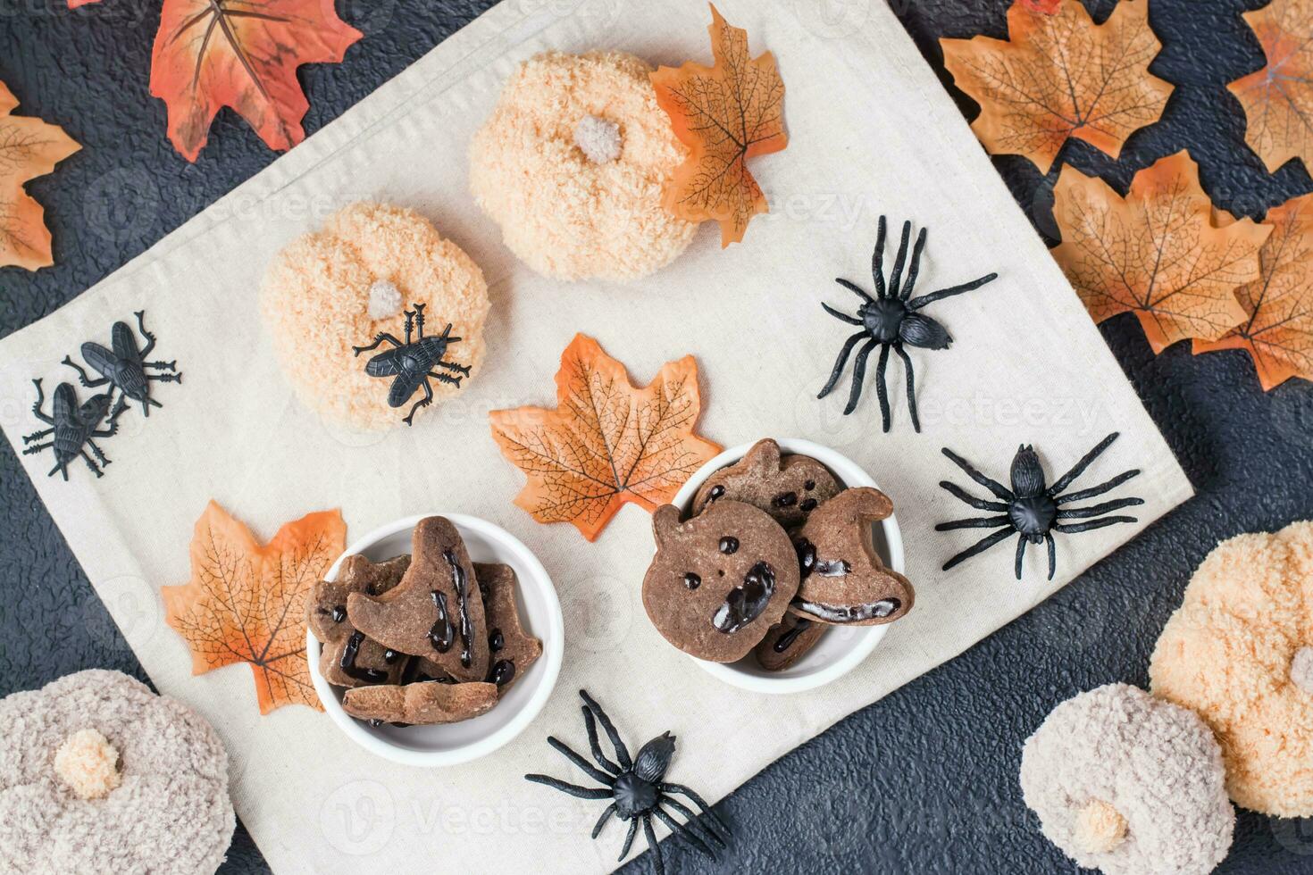 een heerlijk halloween traktatie - peperkoek koekjes met chocola suikerglazuur in kommen Aan een tafel met pompoenen, bladeren en spinnen. traditioneel feesten. top visie foto