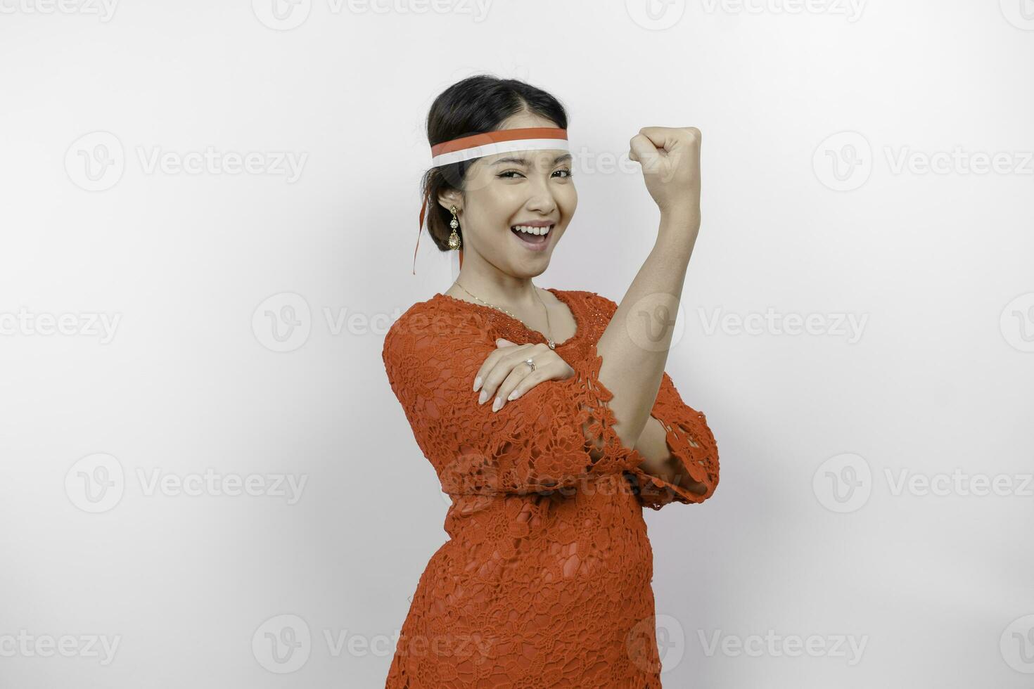 opgewonden Aziatisch vrouw vervelend een rood kebaya en hoofdband tonen sterk gebaar door hijs- haar armen en spieren glimlachen trots. Indonesië's onafhankelijkheid dag concept. foto