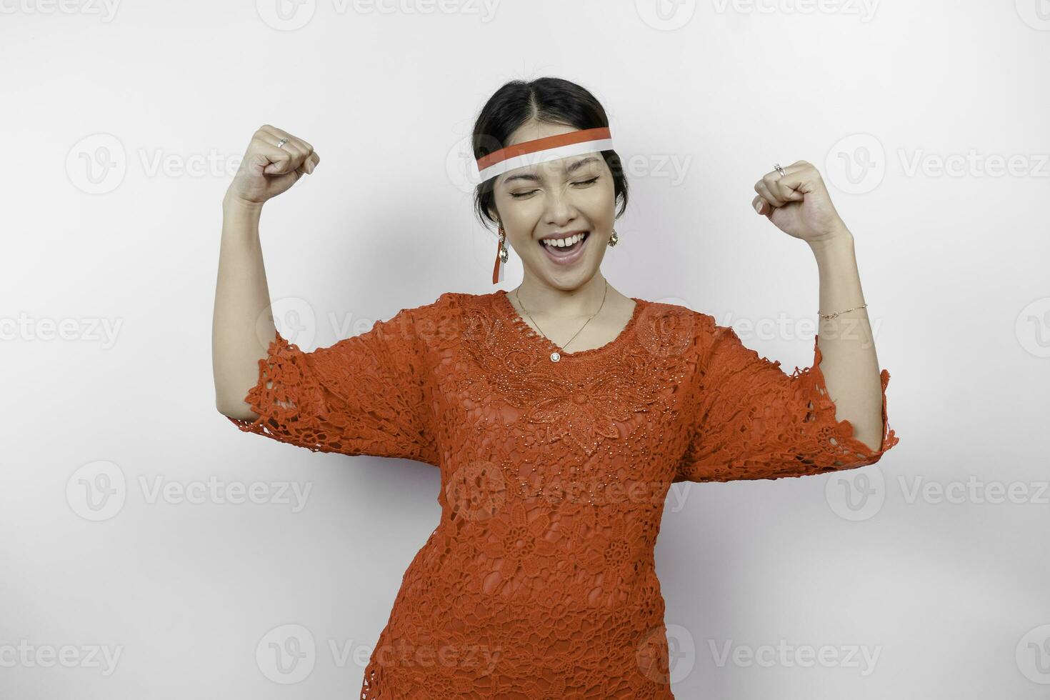 opgewonden Aziatisch vrouw vervelend een rood kebaya en hoofdband tonen sterk gebaar door hijs- haar armen en spieren glimlachen trots. Indonesië's onafhankelijkheid dag concept. foto