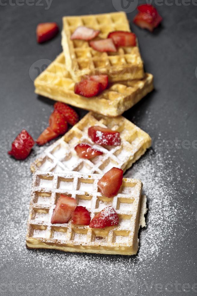 belgische wafels met aardbeien en suikerpoeder op zwart bord. foto