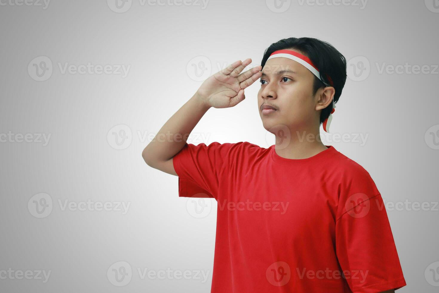 portret van aantrekkelijk Aziatisch Mens in t-shirt met rood en wit lint Aan hoofd, geven groet houding met hand- gedurende Indonesisch vlag ceremonie foto