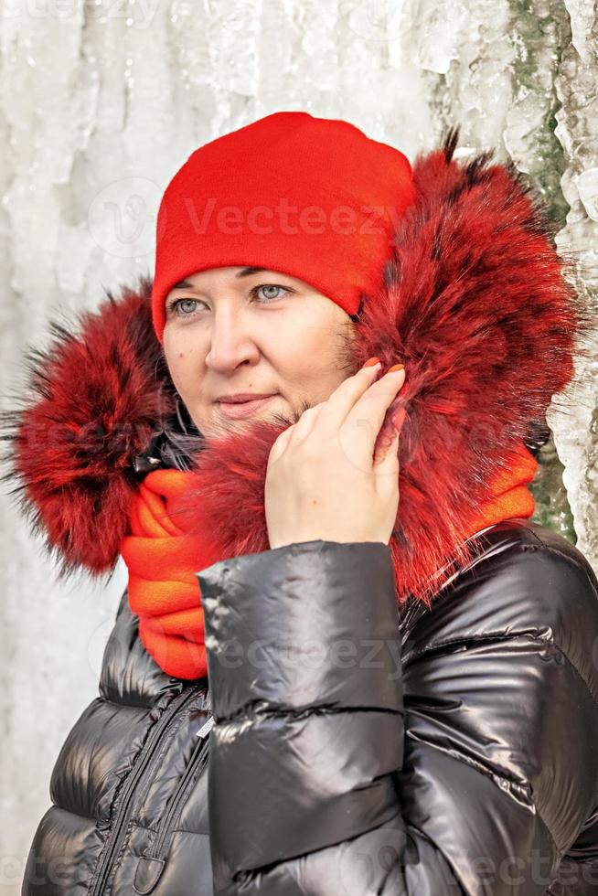 portret van een vrouw in een rode muts en sjaal, warme jas tegen de achtergrond van een ijsmuur. winter foto