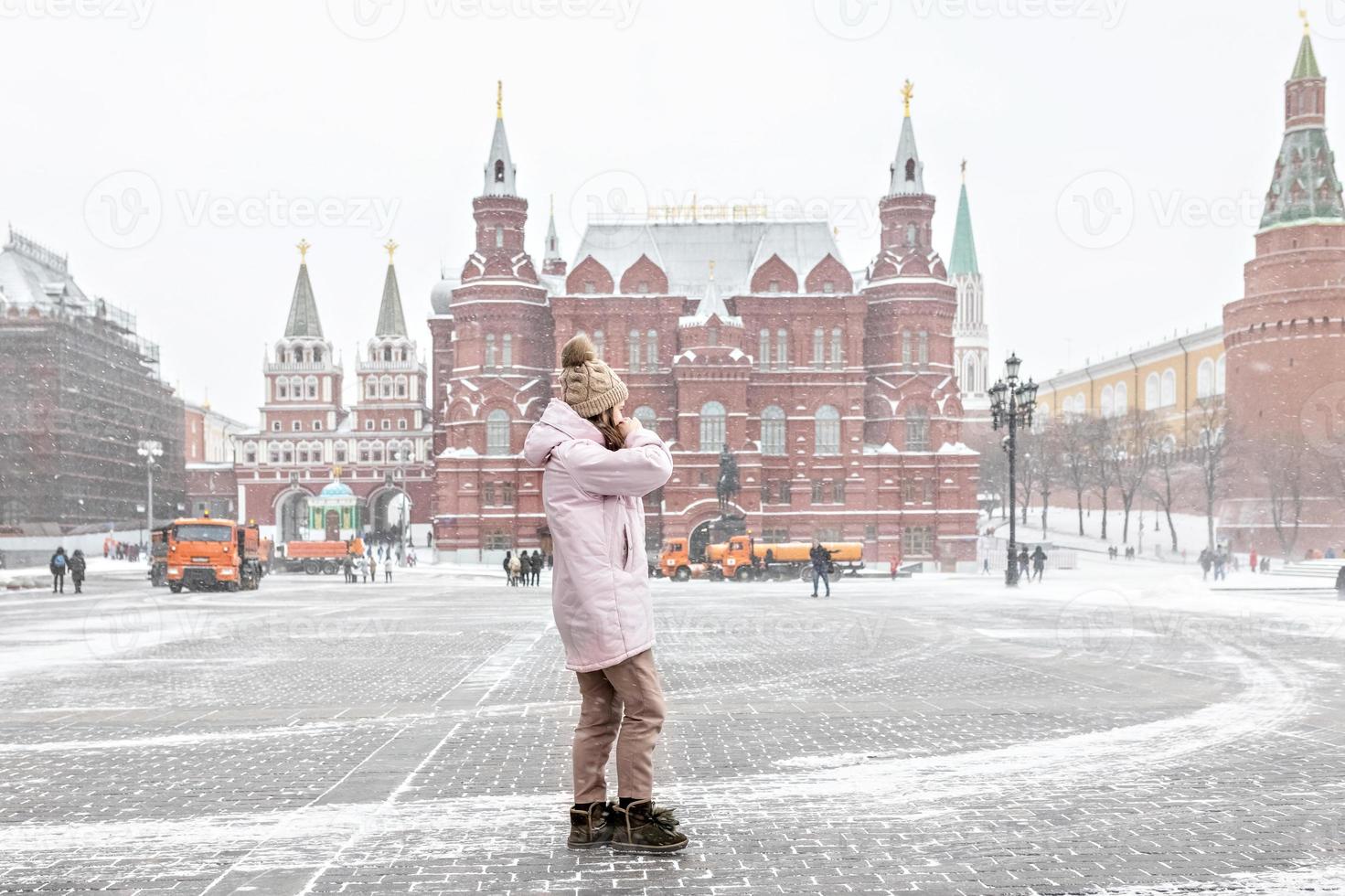 een mooi jong meisje in een roze jas loopt langs het manezhnaya-plein in moskou tijdens een sneeuwval en sneeuwstorm. sneeuwblazers werken op de achtergrond. foto