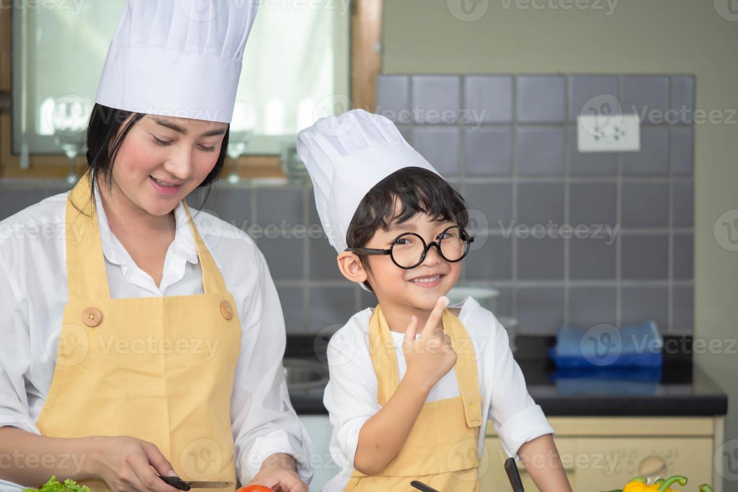 Aziatische vrouw jonge moeder met zoon jongen koken salade eten met groente bedrijf tomaten en wortelen, paprika op plaat voor gelukkig gezin koken eten genieten levensstijl keuken in huis foto