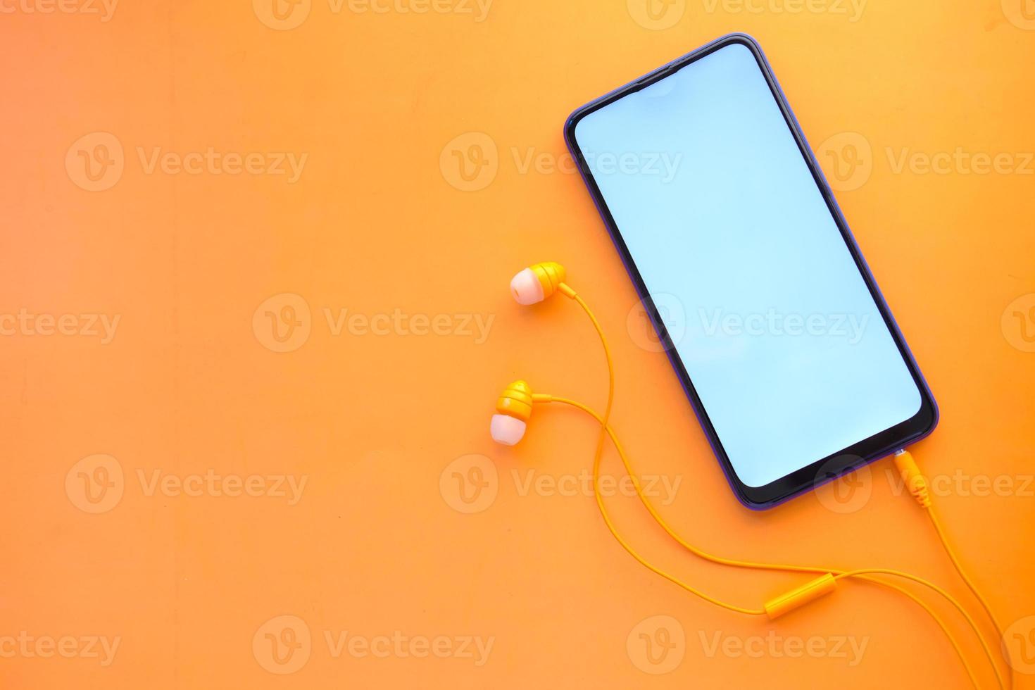 slimme telefoon met leeg scherm, oortelefoon op oranje achtergrond foto