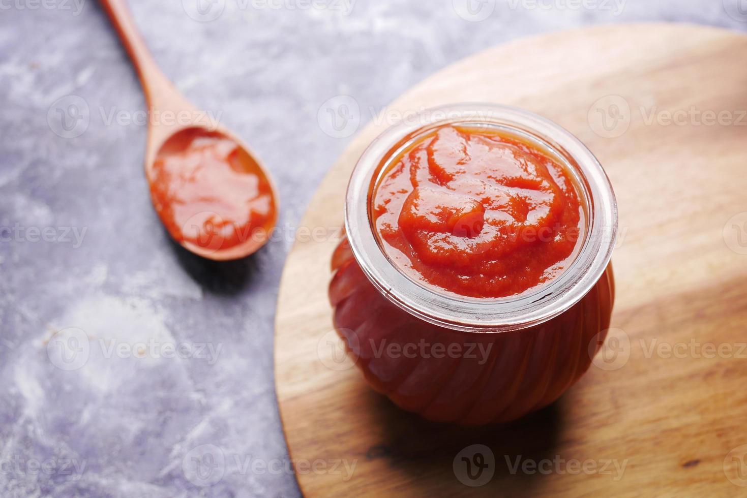tomatensaus in een klein potje met verse tomaat op tafel foto