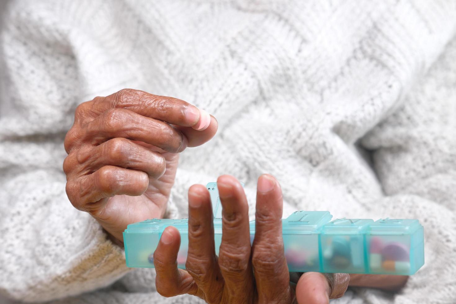 Senior vrouwenhanden die medicijnen uit een pillendoos nemen foto