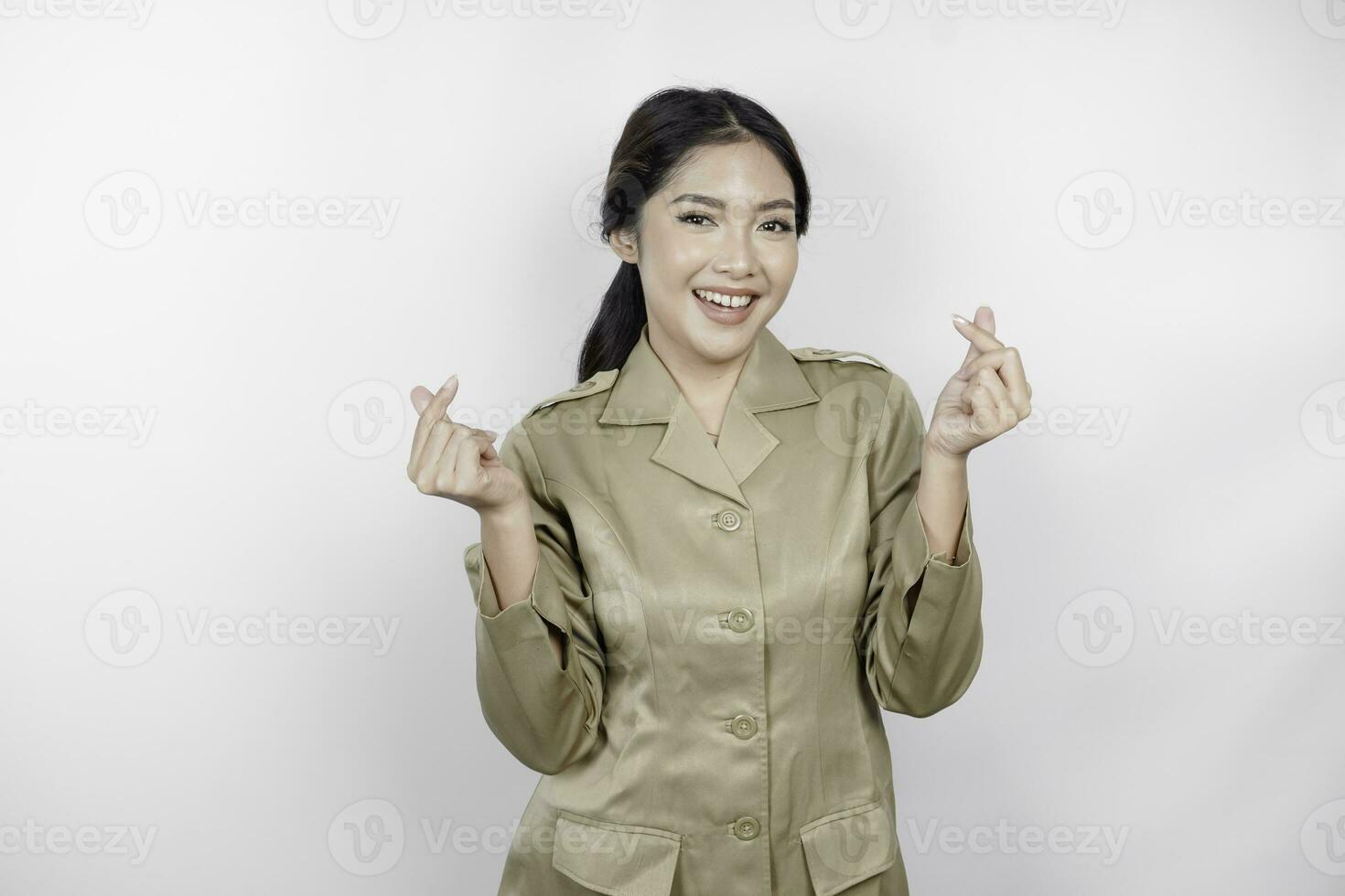 een jong Aziatisch vrouw in bruin khaki uniform tonen inschrijving gevoel door vormgeven hart met haar vingers. Indonesisch regering arbeider. foto