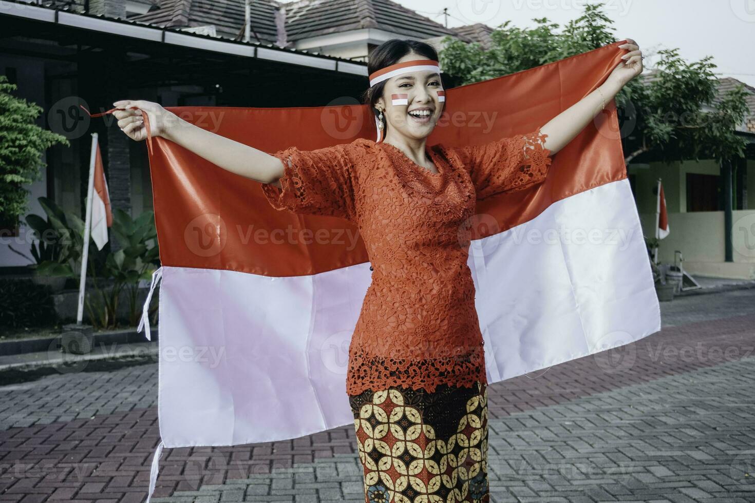 gelukkig glimlachen Indonesisch vrouw vervelend rood kebaya Holding Indonesië's vlag naar vieren Indonesië onafhankelijkheid dag. buitenshuis fotoshoot concept foto