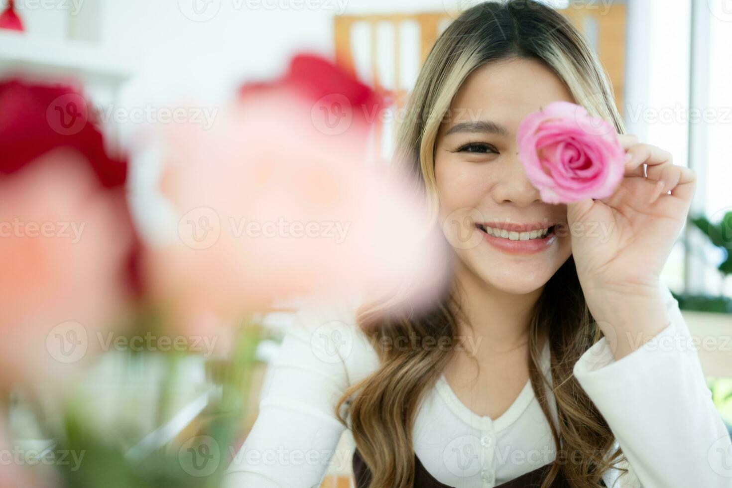 glimlachen Aziatisch vrouw Holding roze bloem in haar hand- Bij huis foto