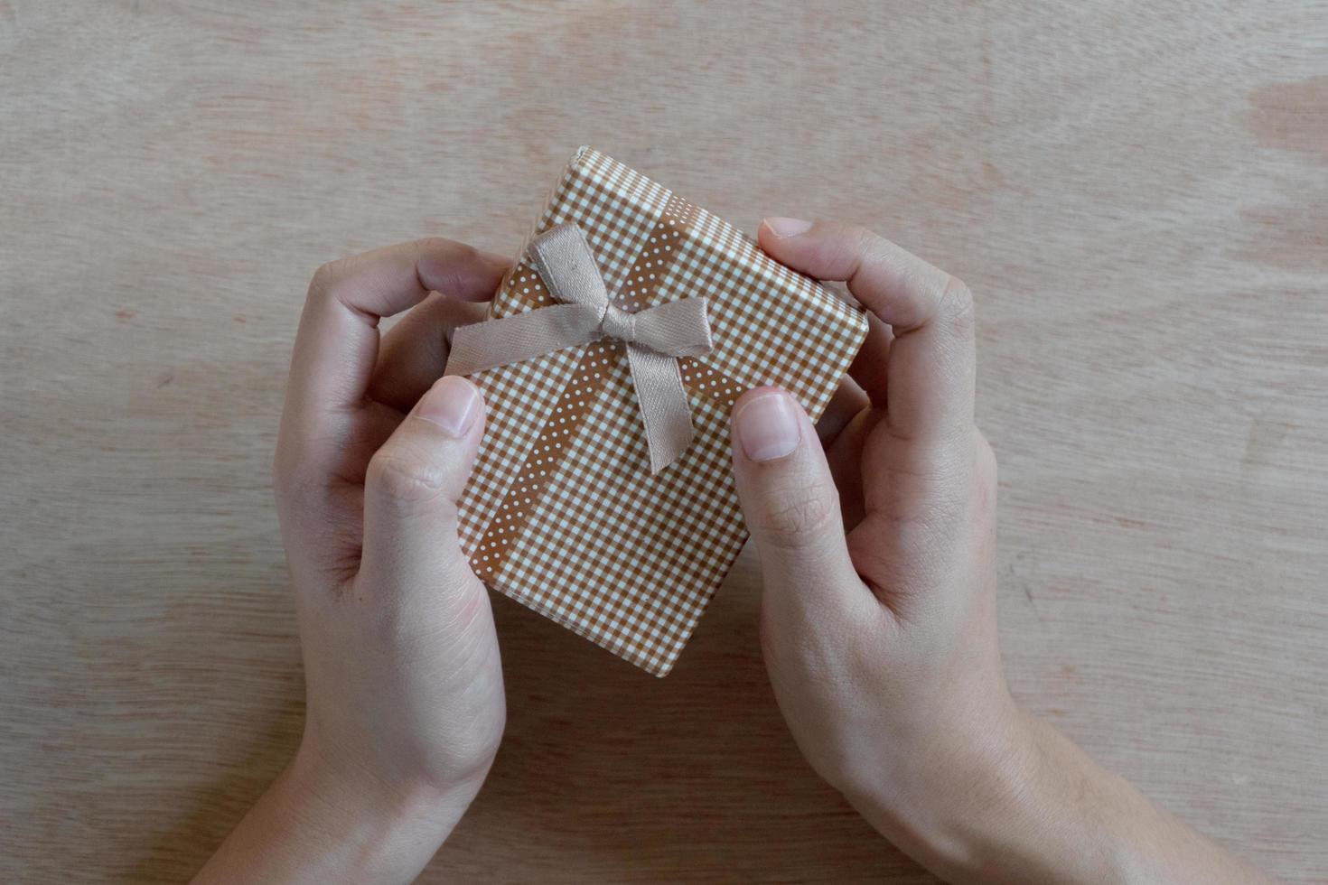 close-up shot van vrouwelijke handen met een klein cadeautje. klein cadeautje in de handen van een vrouw binnen. foto