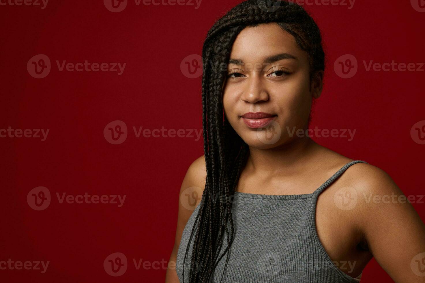 detailopname portret van een charmant jong Afrikaanse vrouw met elegant traditioneel dreadlocks, schattig glimlachen op zoek Bij camera, geïsoleerd over- rood achtergrond met kopiëren ruimte foto