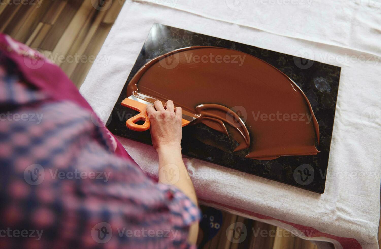 top visie van chocolatier Holding taart schraper en koeling gesmolten chocola massa Aan een marmeren tafel foto