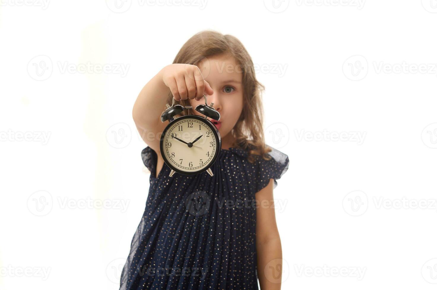 zacht focus Aan een zwart alarm klok in de hand- van een mooi mooi verrast baby meisje in avond jurk, poseren tegen wit achtergrond met kopiëren ruimte. zwart vrijdag concept foto